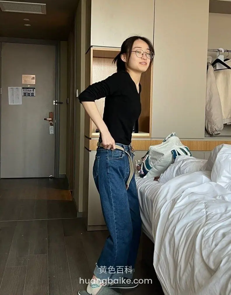 酒店房间里手插裤袋站立，床和柜子在身后
