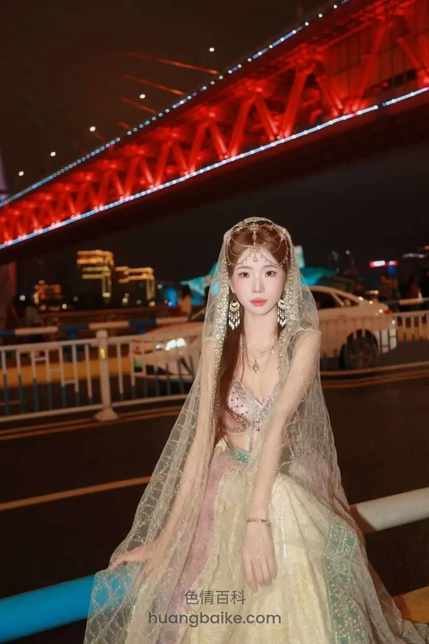夜晚桥边穿着婚纱坐着，身后红桥灯光亮着