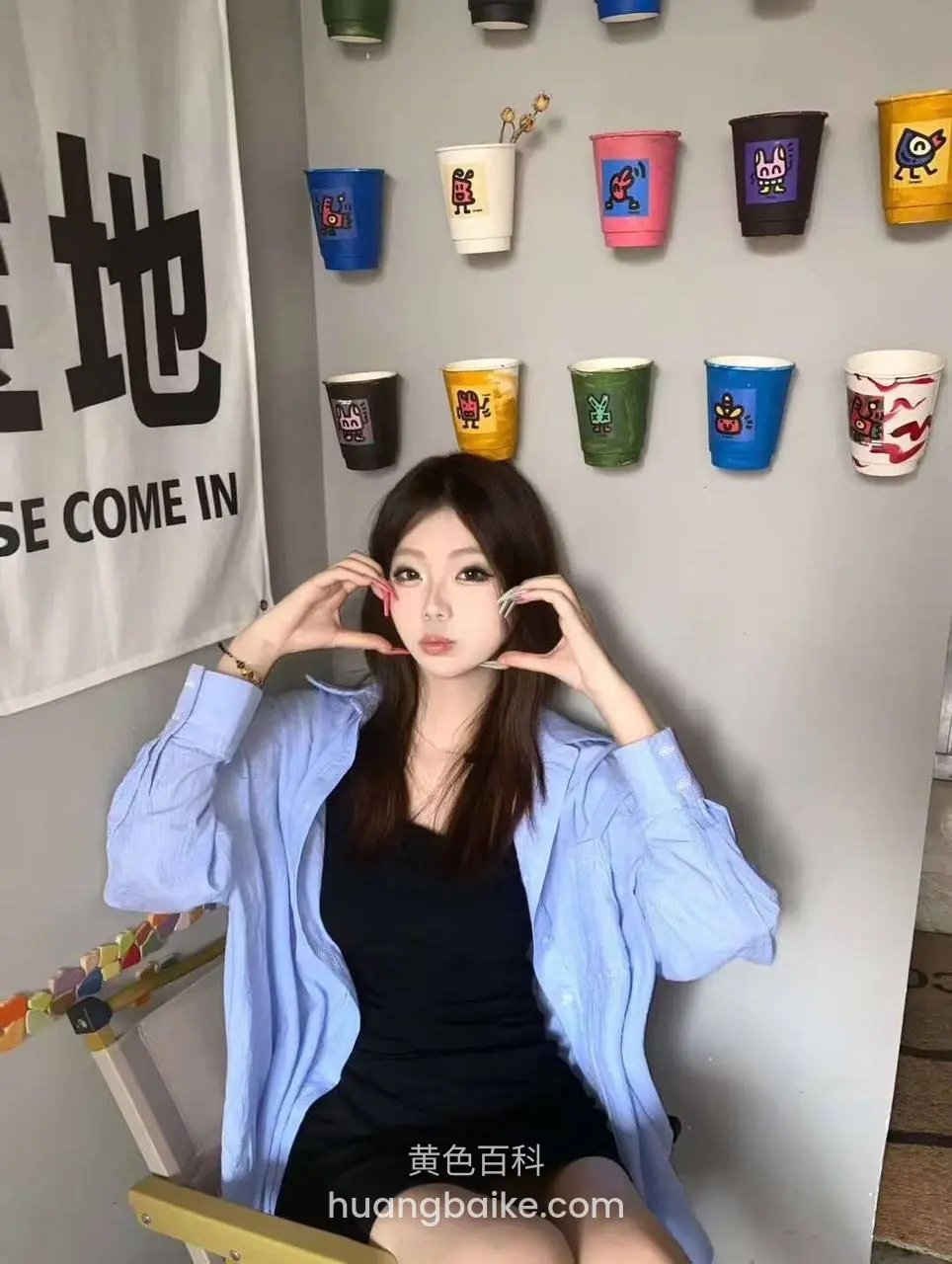 咖啡馆墙上挂满彩色杯子，坐椅上双手比心