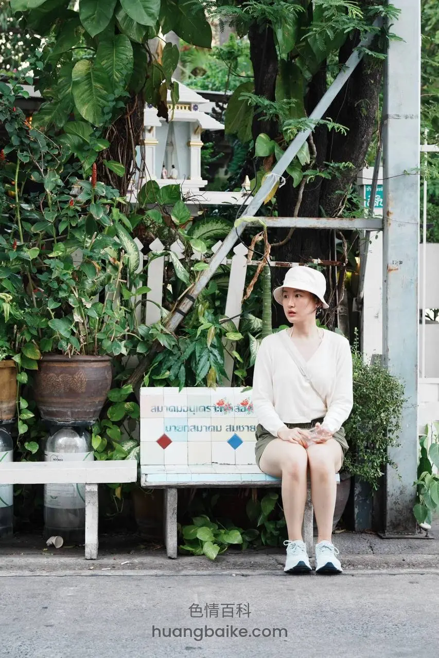 路边白长椅上坐着身后是绿植和神龛