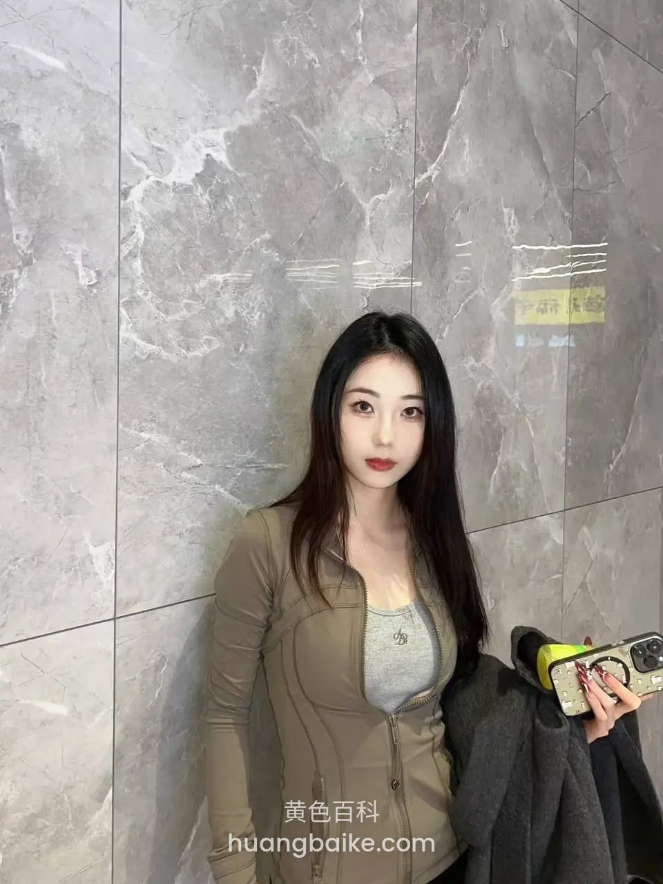 靠大理石墙壁站立，左手拿着手机和外套