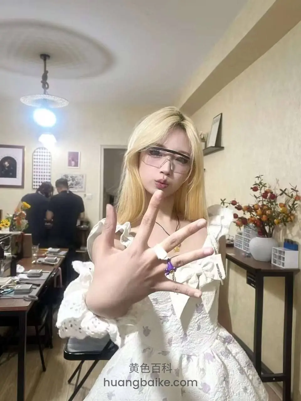 室内举手比剪刀手，身后有人在忙