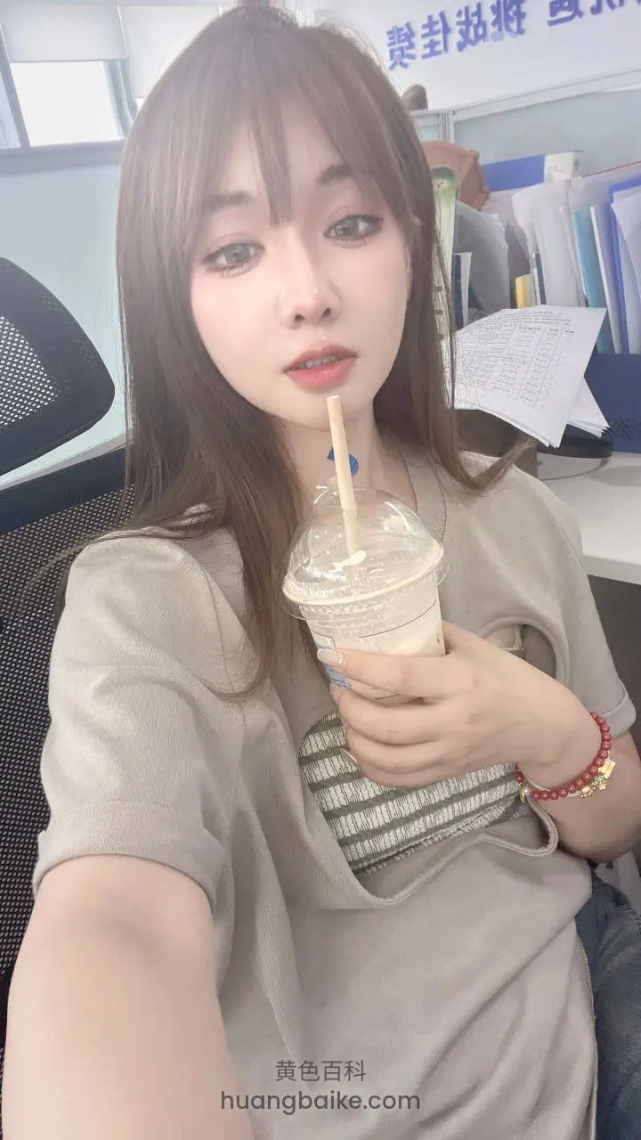 拿着奶茶杯，背景墙上有蓝字标识