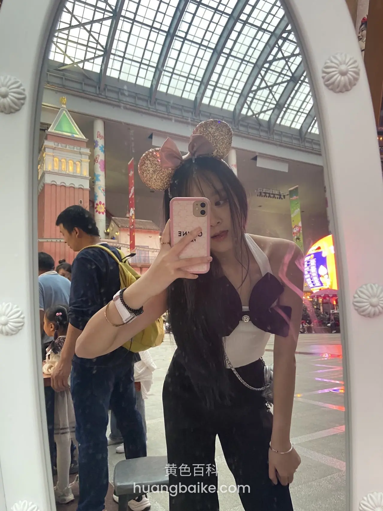 商场拱门前举着手机，身后游客和建筑