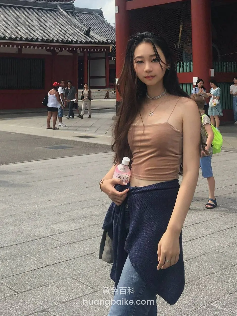 寺庙前长发女子手拿饮料披深蓝外套