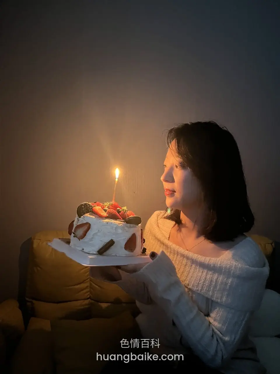 沙发上端着生日蛋糕，蜡烛点亮