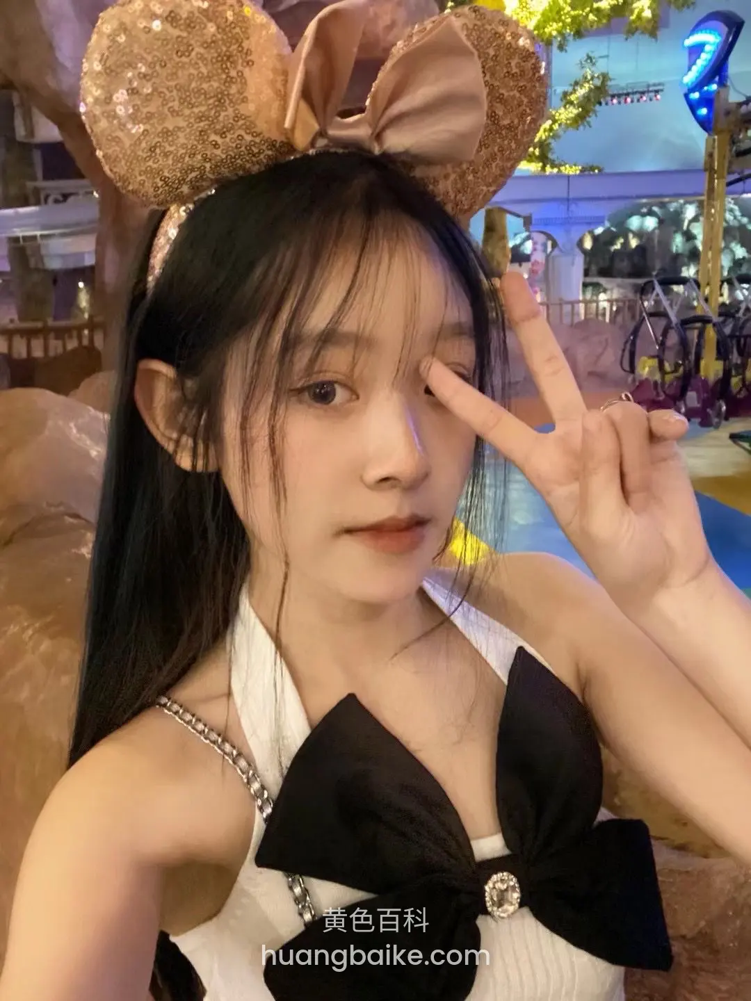 游乐园拿着米妮耳朵头饰比剪刀手，身后有摩天轮