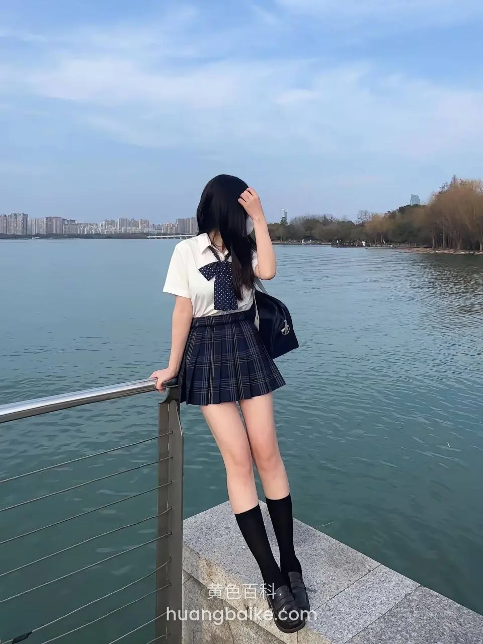 湖边栏杆前站立，手扶栏杆抬头看湖面，背包斜挎肩上