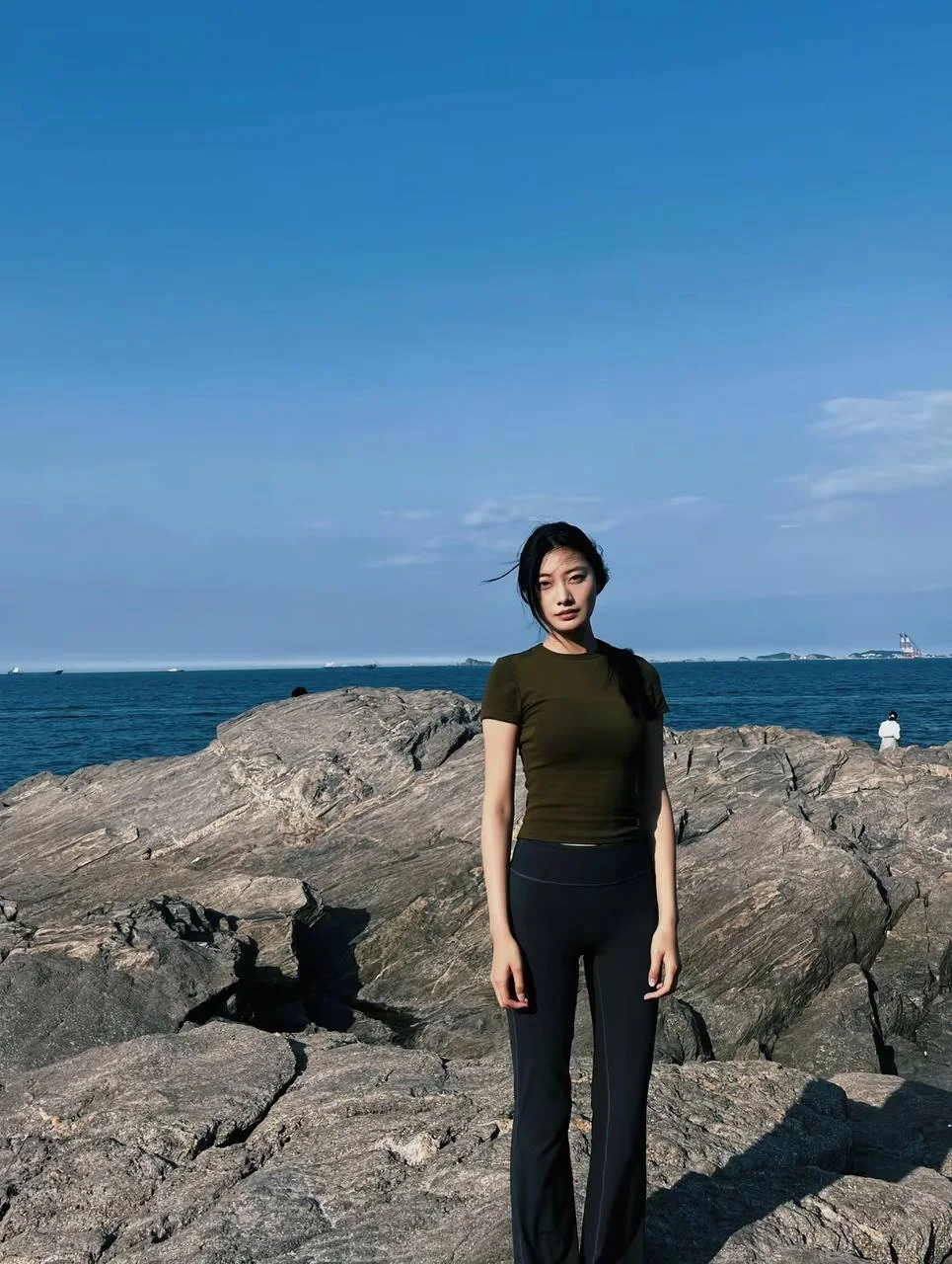 女生站在海边礁石上 身后是蓝天大海