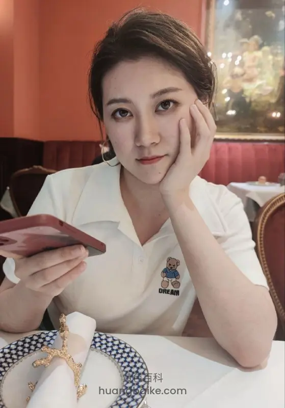 餐厅桌前托腮看镜头，手里拿着手机