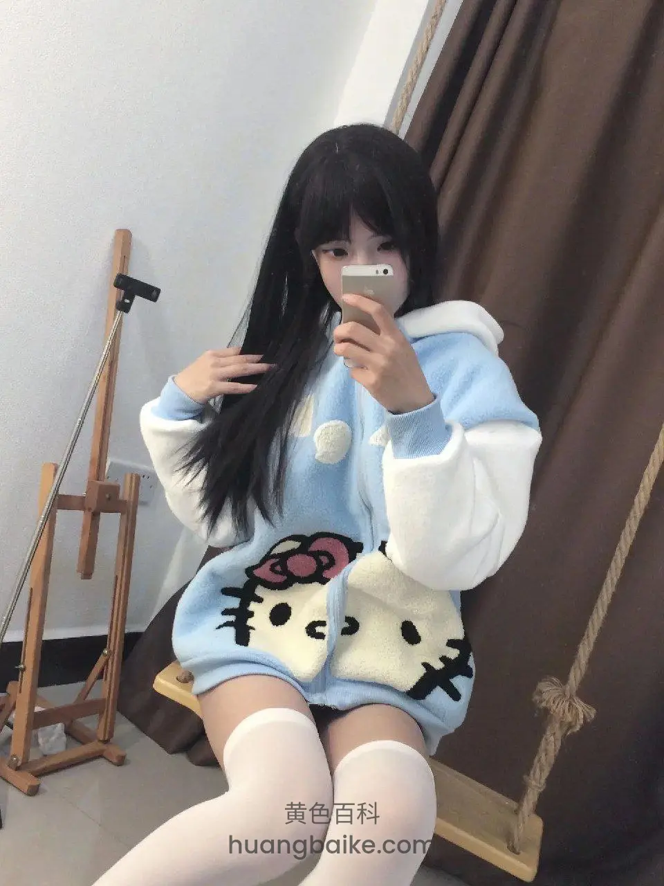 室内木秋千上拿着手机自拍，身后有画架