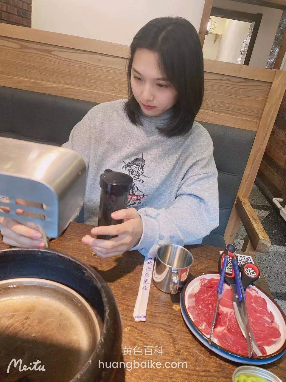 餐厅桌前拿着手机，桌上火锅肉盘和调料