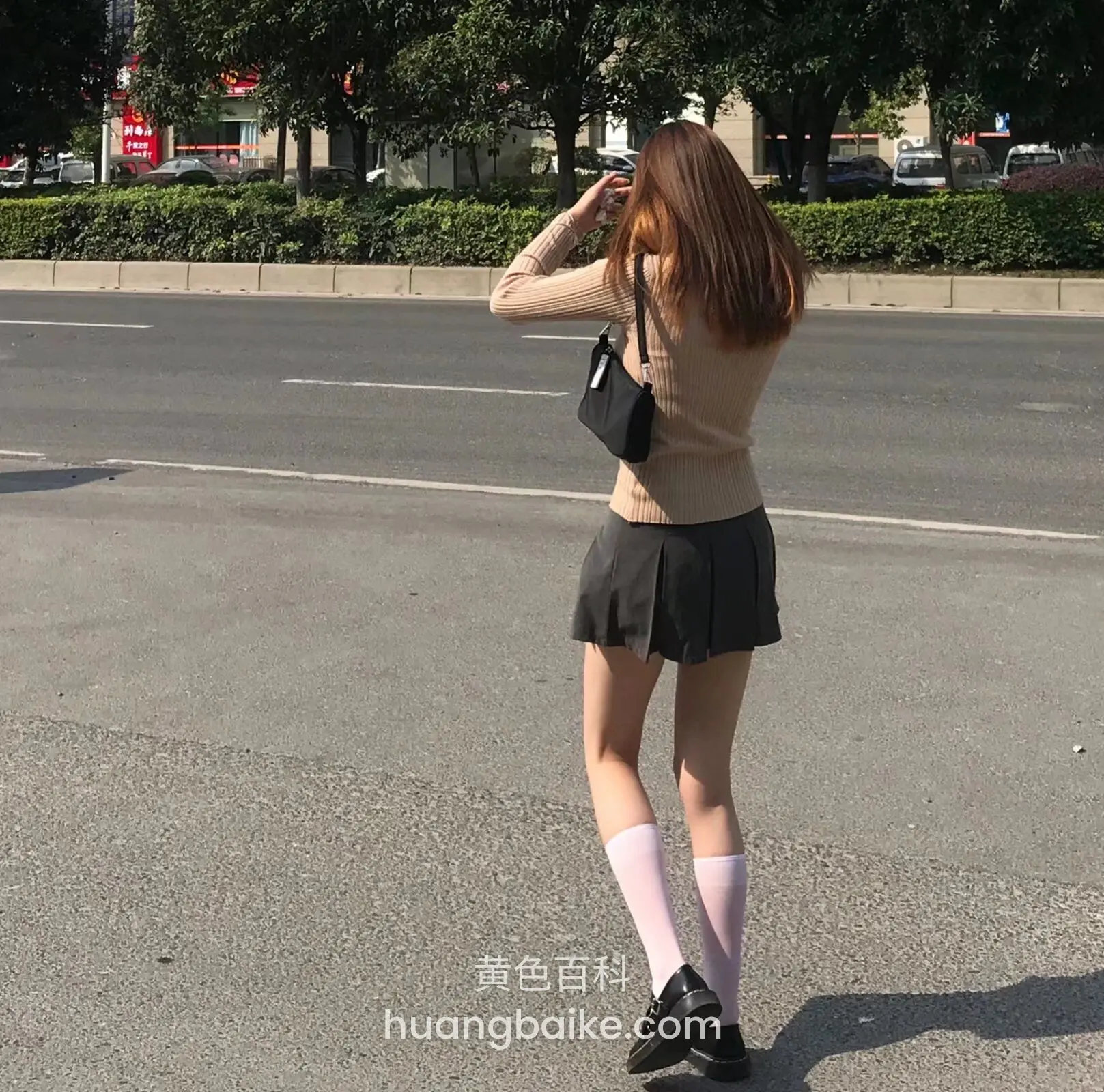 路中间背对镜头拍照，旁边是绿化带