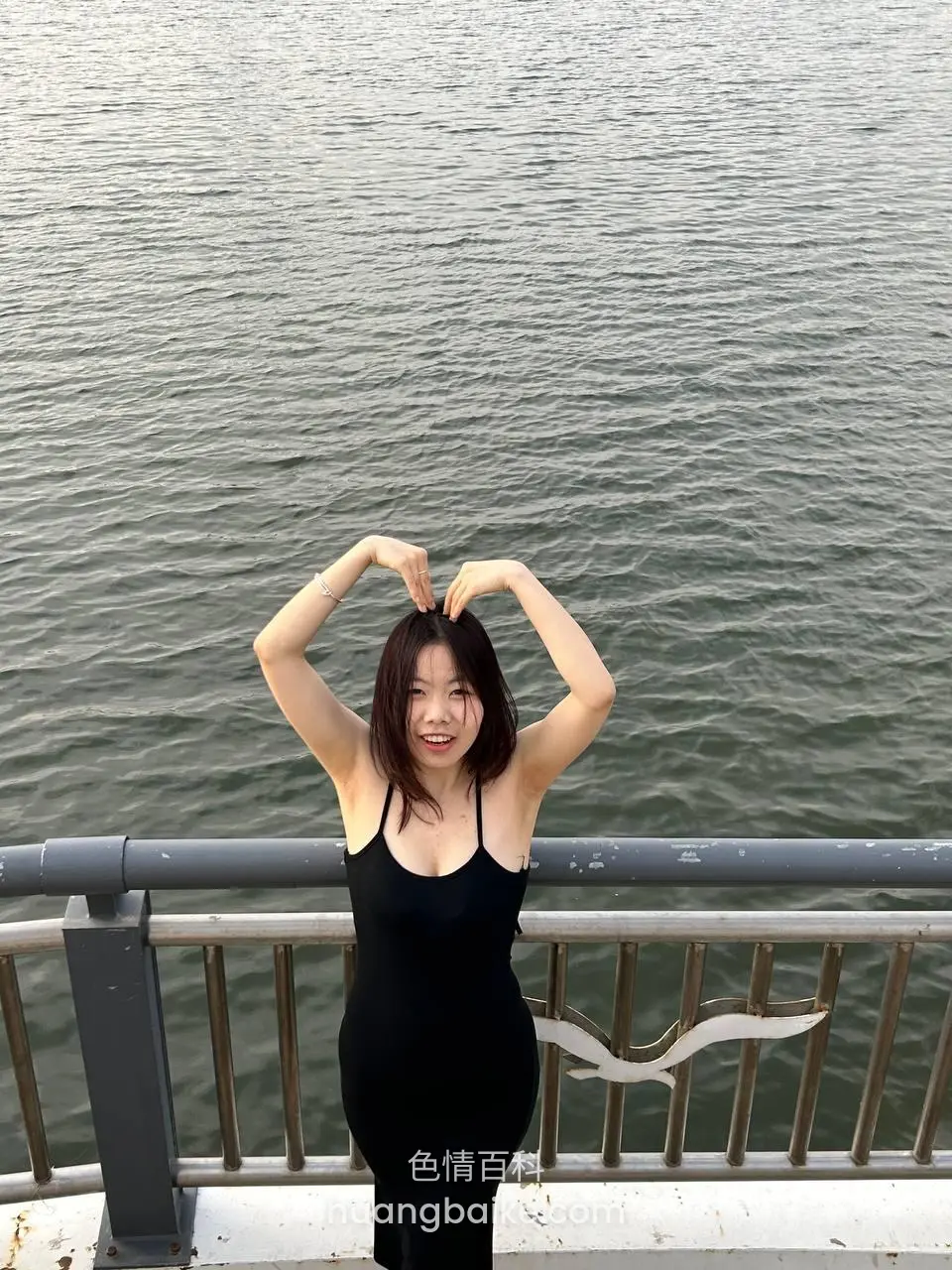 江边栏杆前摆心形手势，镜头对着水面