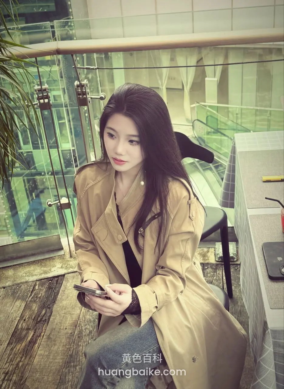 商场二楼露台坐着玩手机，身后玻璃栏杆和扶梯