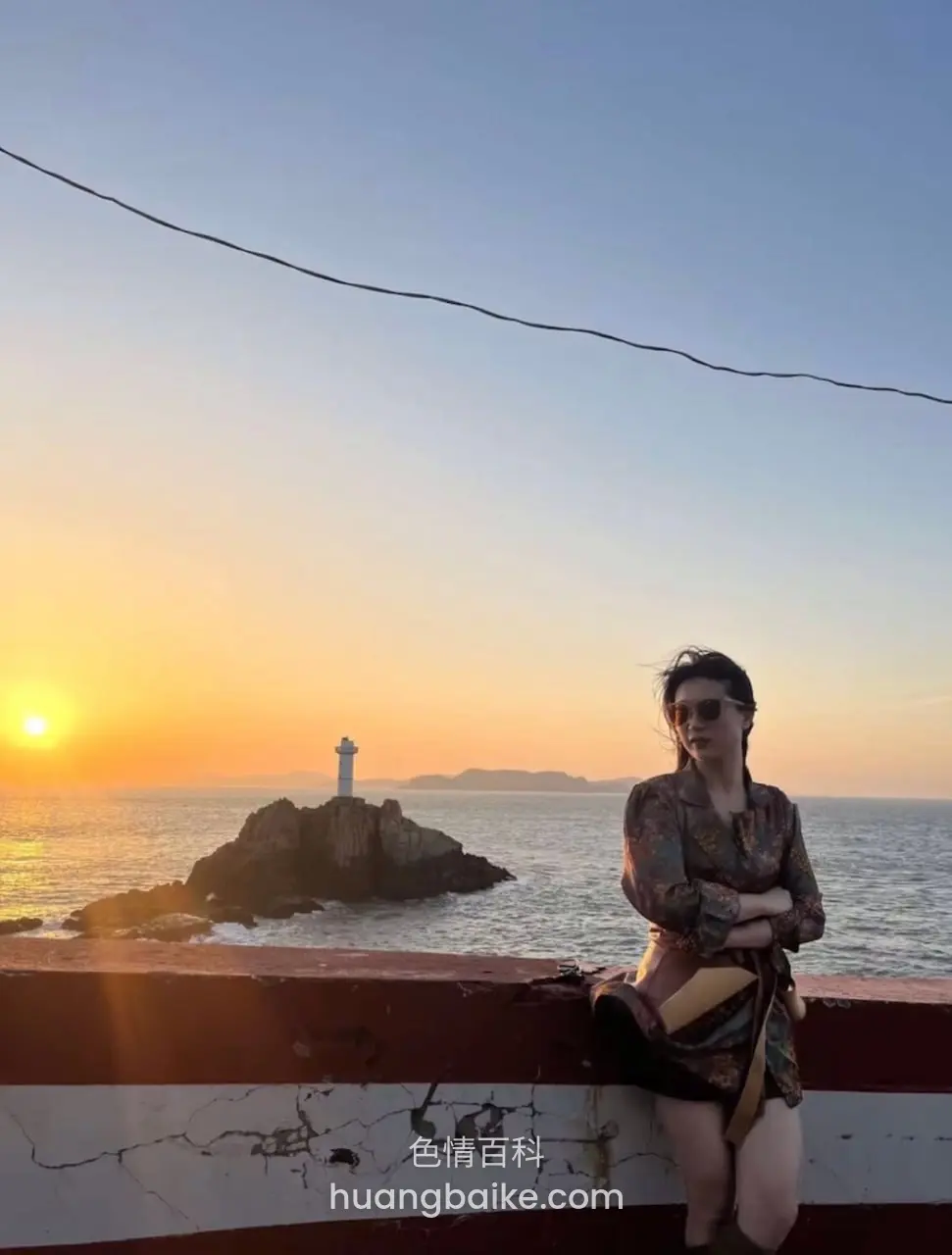 靠着海边红色栏杆看日落，远处礁石上灯塔