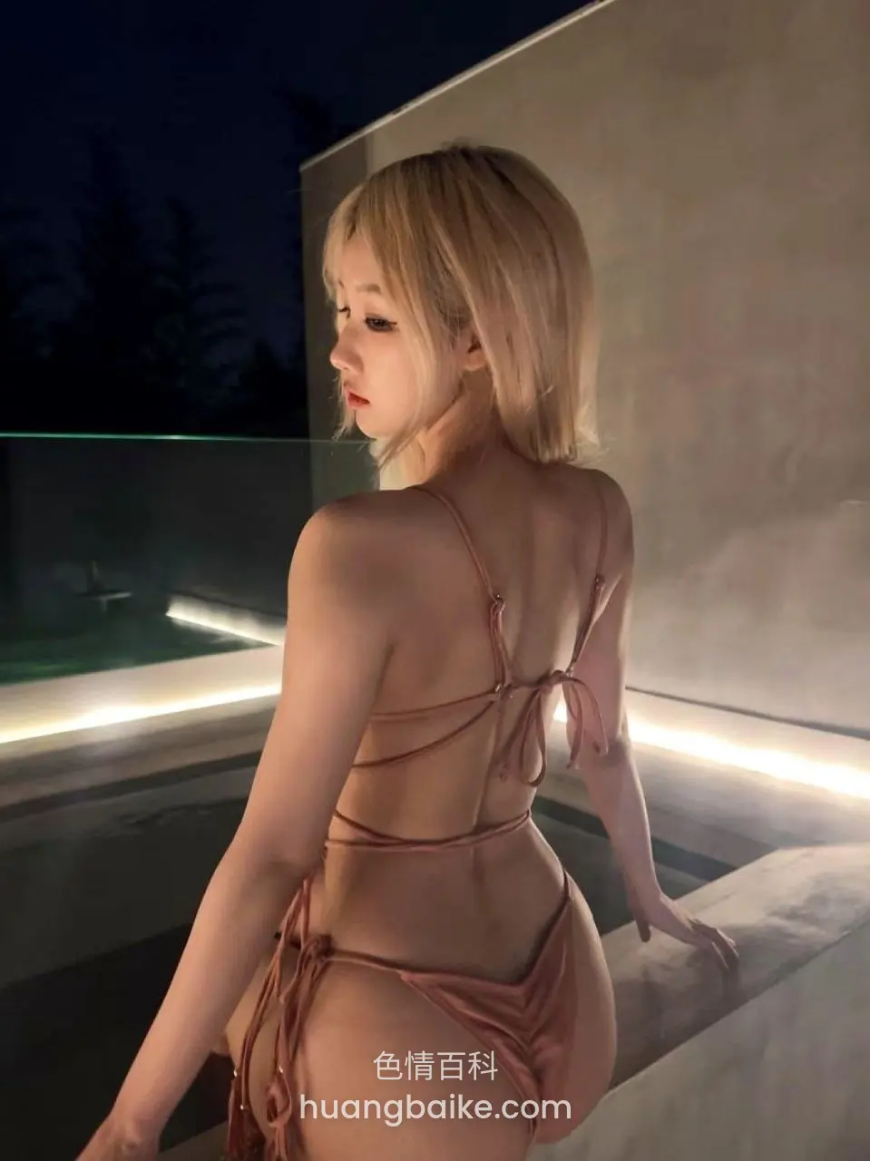 夜间泳池边转身背对镜头，身上粉色绑带泳装