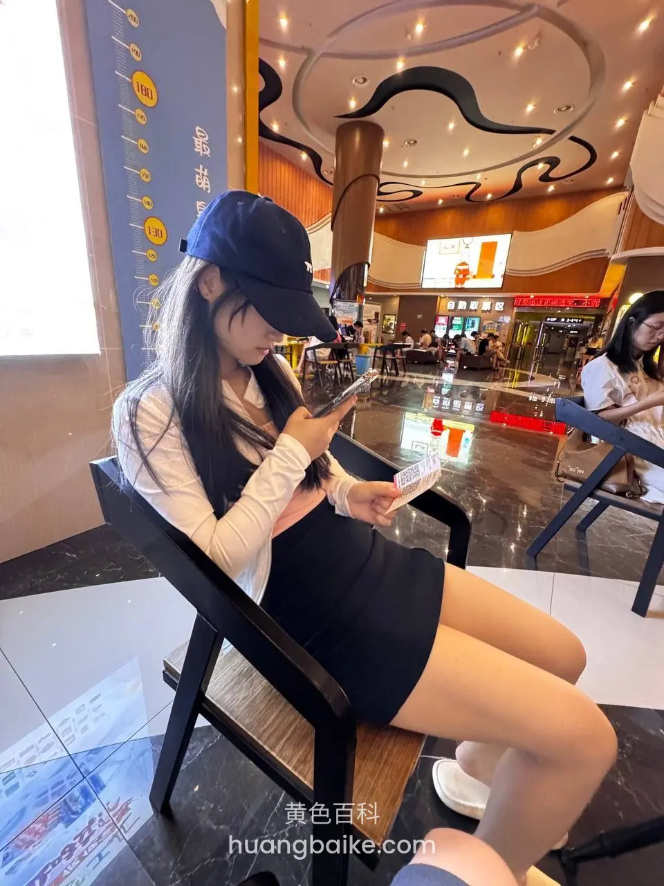 椅子上低头玩手机，手里拿着两张纸牌