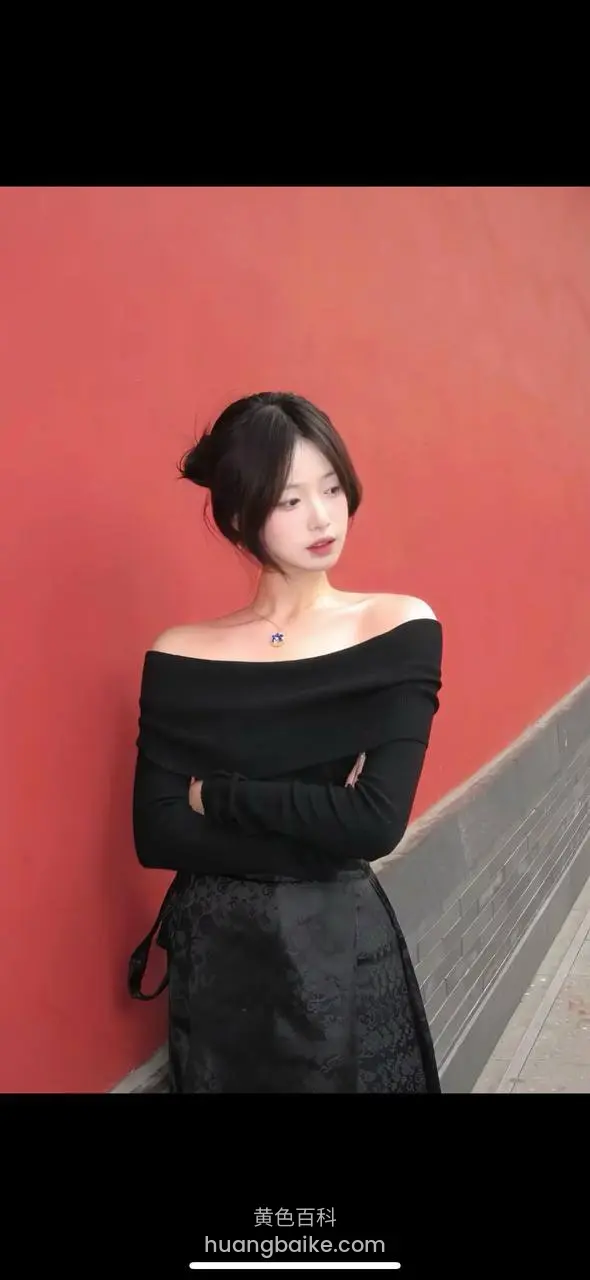 靠红墙低头看旁边，黑色抹胸长裙手拿包