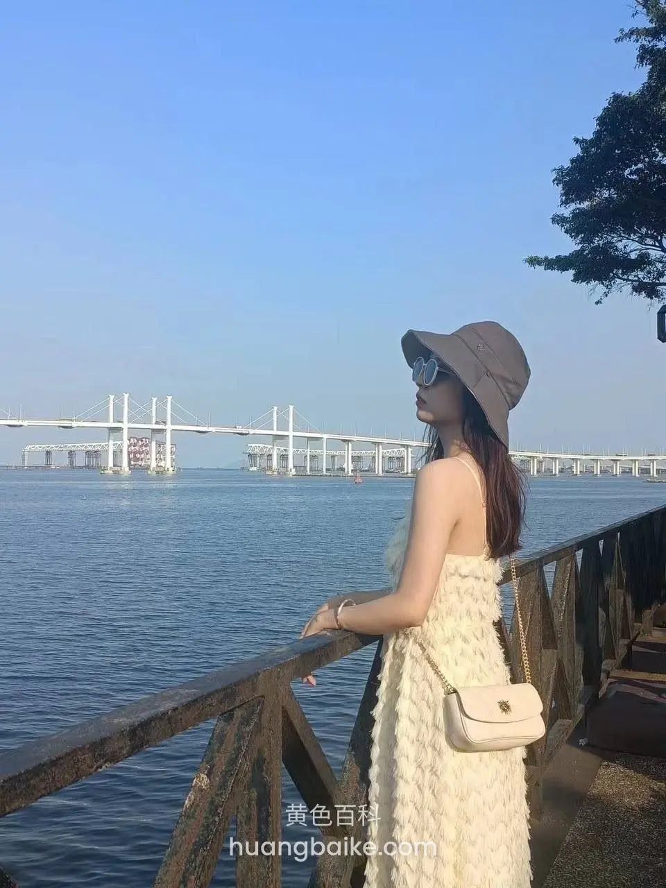 海边栏杆边远眺大桥，戴着帽子和墨镜