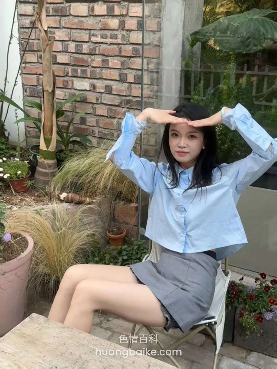 花园里坐着摆手势比心，身后砖墙和花盆