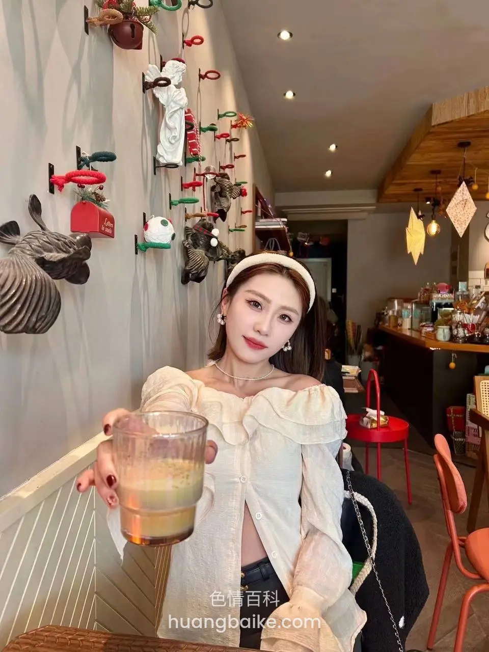 咖啡店墙边举着饮料杯，旁边挂满装饰玩偶
