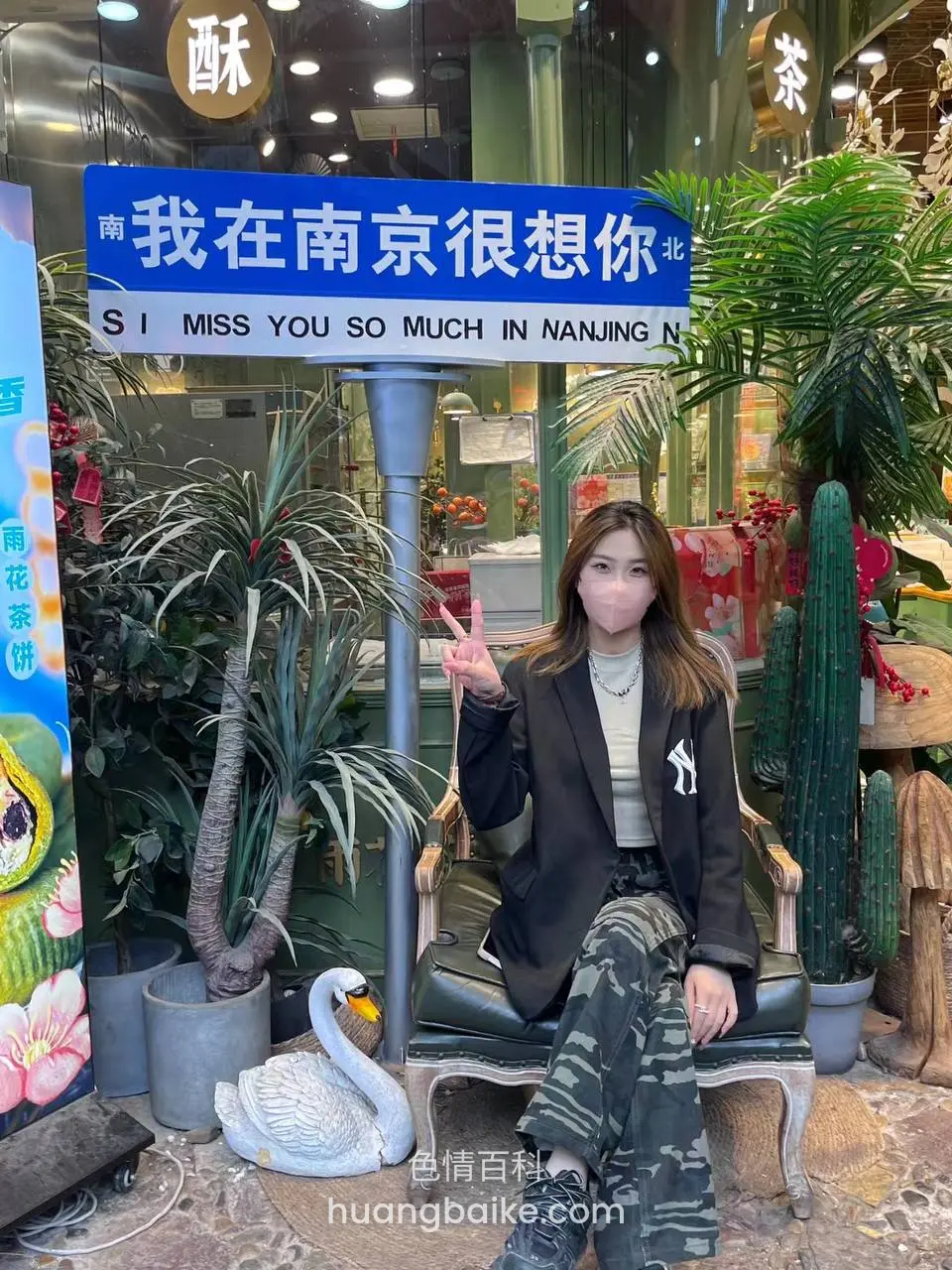 店门口蓝牌下坐着比剪刀手，牌子上写我在南京很想你