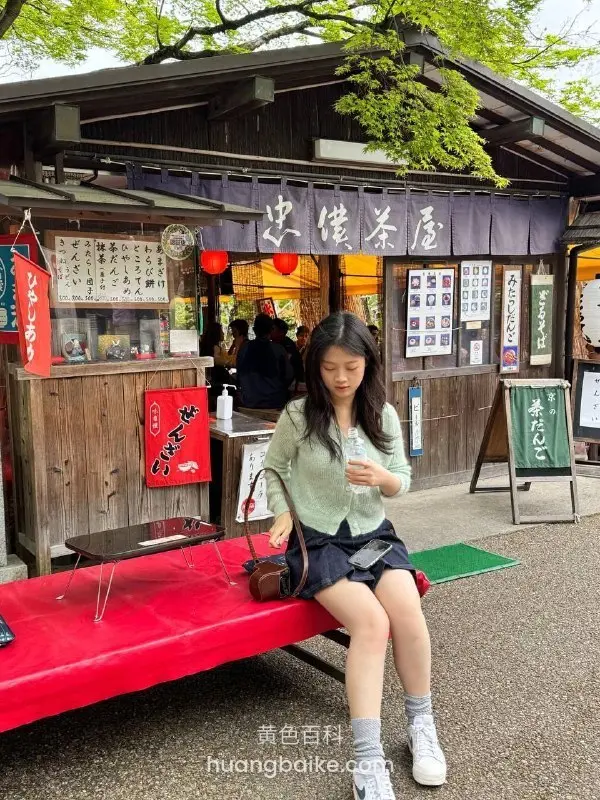 茶屋前红长椅上拿着手机，身后日式招牌和横幅