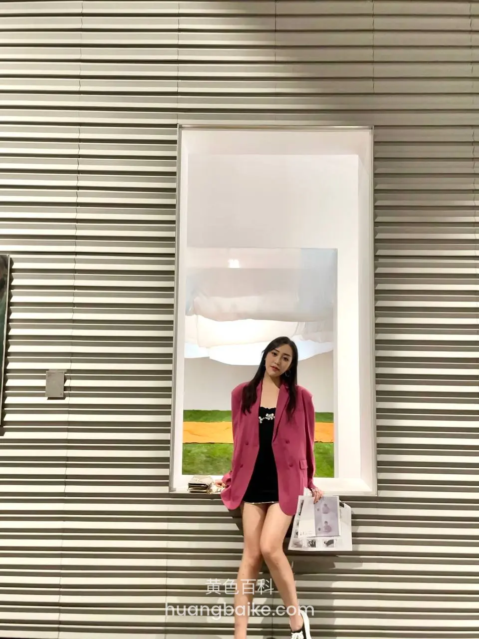 靠在条纹墙边窗口，手拿购物袋看镜头