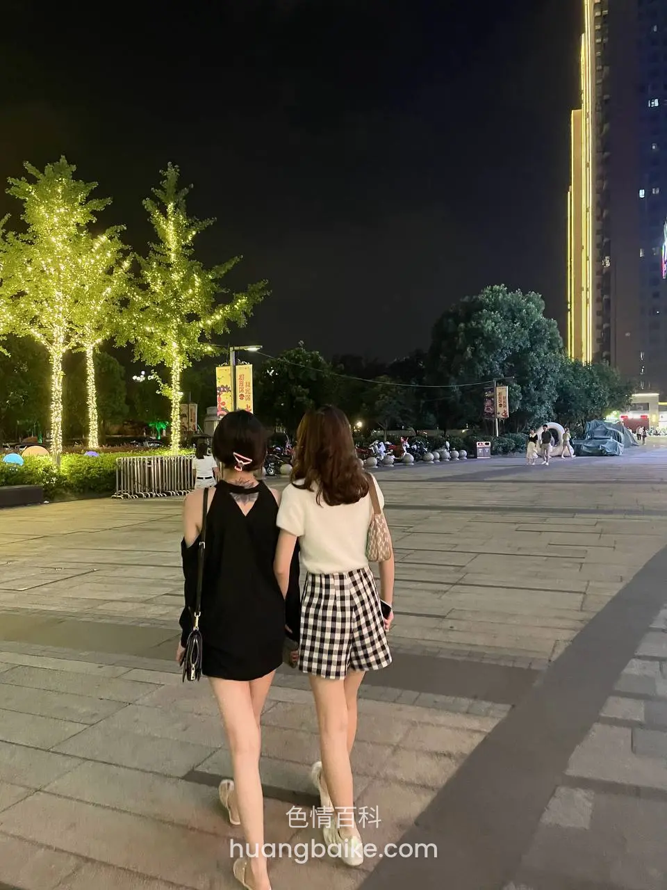 夜晚广场上两人并肩走着，身后是灯树