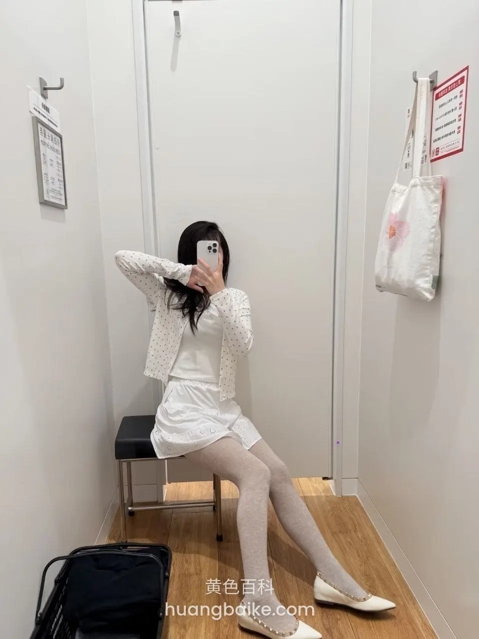试衣间里举手机拍全身，身后挂着白袋子