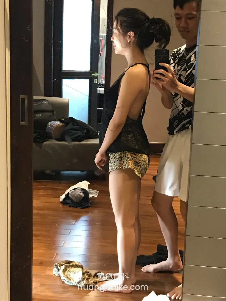 房间里侧身站立，身后男人举手机